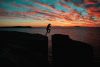 silhouette photo of a man jumps on to cliff near sea during sunset